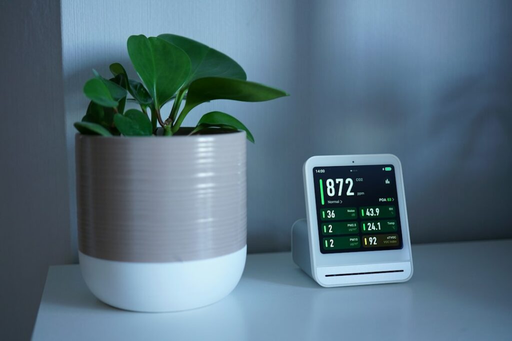 Dispositivo con display che mostra i valori rilevati accanto a una pianta in casa, strumento per il monitoraggio ambientale di case e immobili