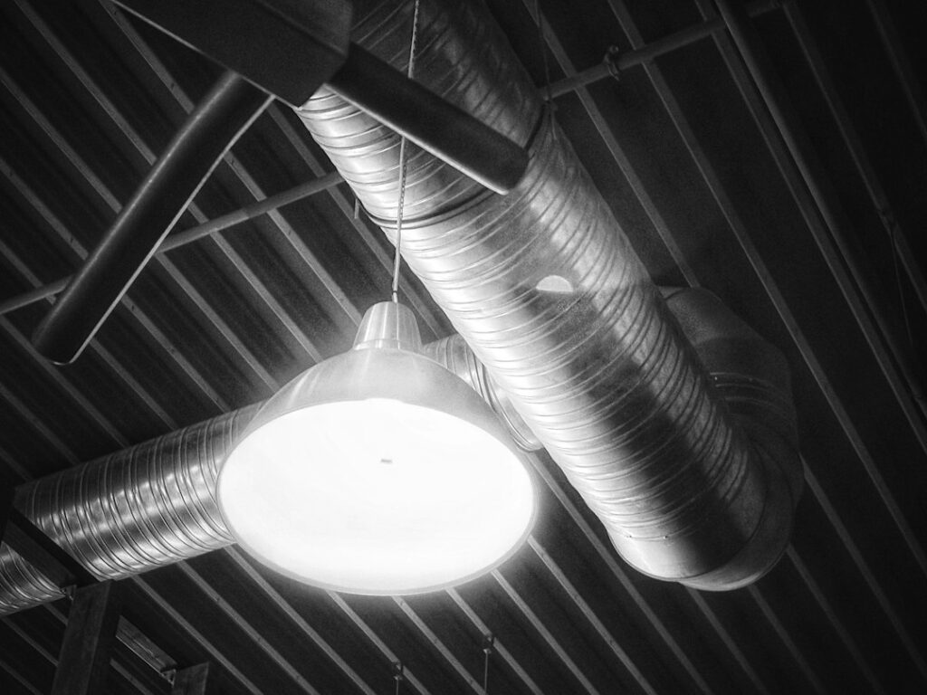 Soffitto industriale con canali di ventilazione e lampada sospesa, elemento centrale dell'igiene industriale negli ambienti di lavoro
