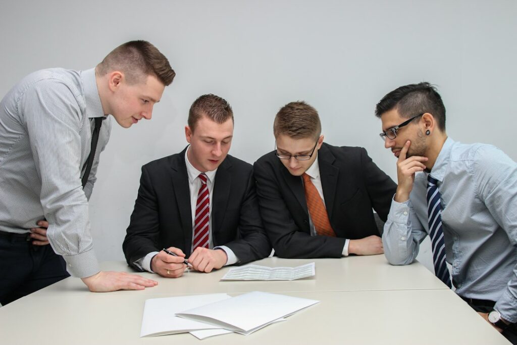 Quattro professionisti riuniti intorno a un tavolo esaminano documenti cartacei durante una consulenza per la valutazione dei rischi