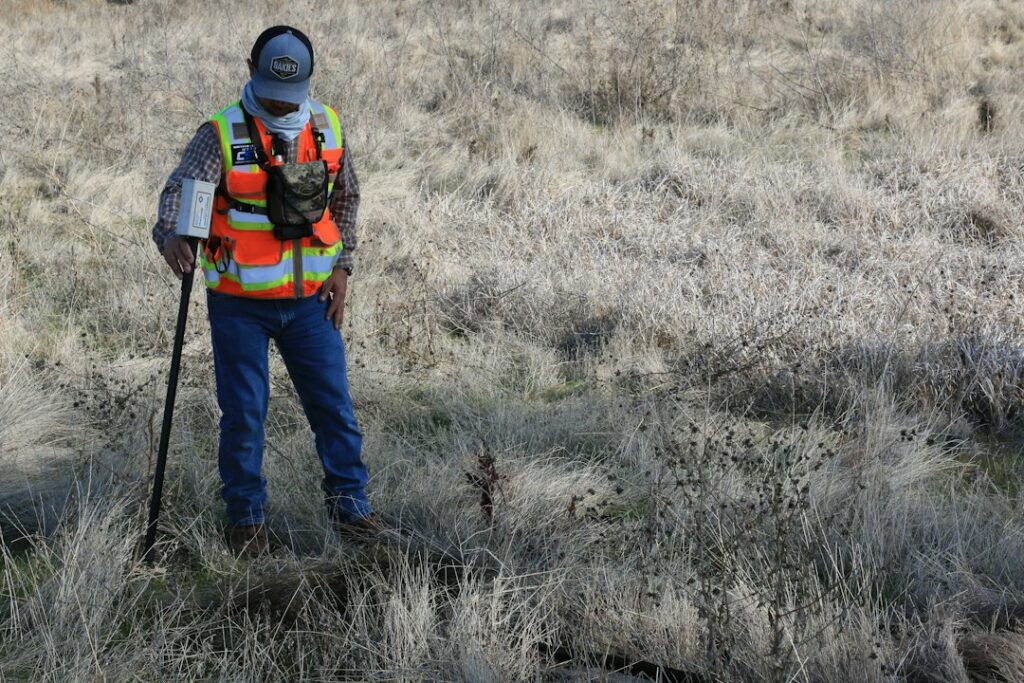 Tecnico con giacca alta visibilità che esegue un rilievo in un campo, attività preliminare alla valutazione di impatto ambientale