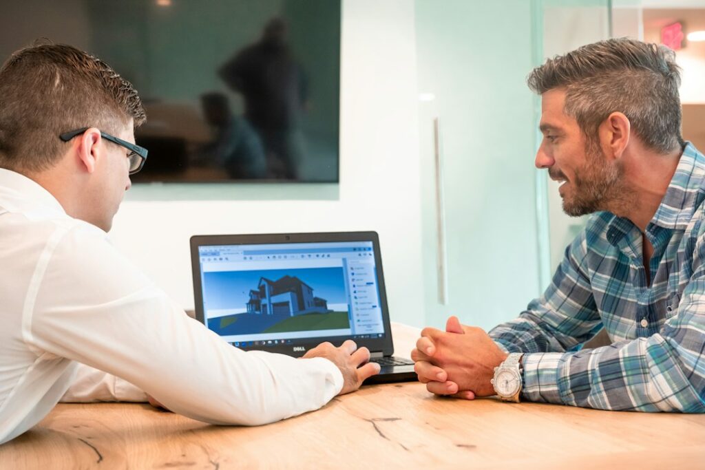 Tecnico e cliente seduti al tavolo esaminano elaborati progettuali durante una consulenza professionale
