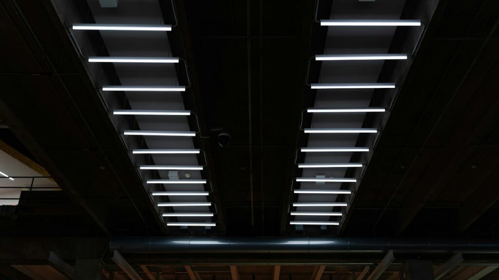 File di lampade fluorescenti accese che illuminano il soffitto scuro di un ambiente di lavoro, riferimento per la valutazione dei rischi da illuminamento
