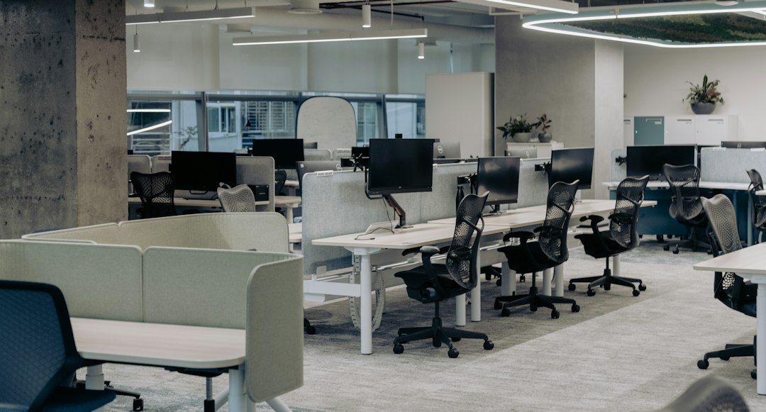 Ufficio open space con scrivanie, computer e sedie ergonomiche separate da divisori bassi, ambiente da analizzare nella valutazione dello stress da lavoro correlato