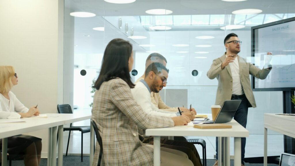 Uomini e donne seduti in sala riunioni ascoltano un relatore che usa uno schermo digitale: la formazione sulla sicurezza in azienda