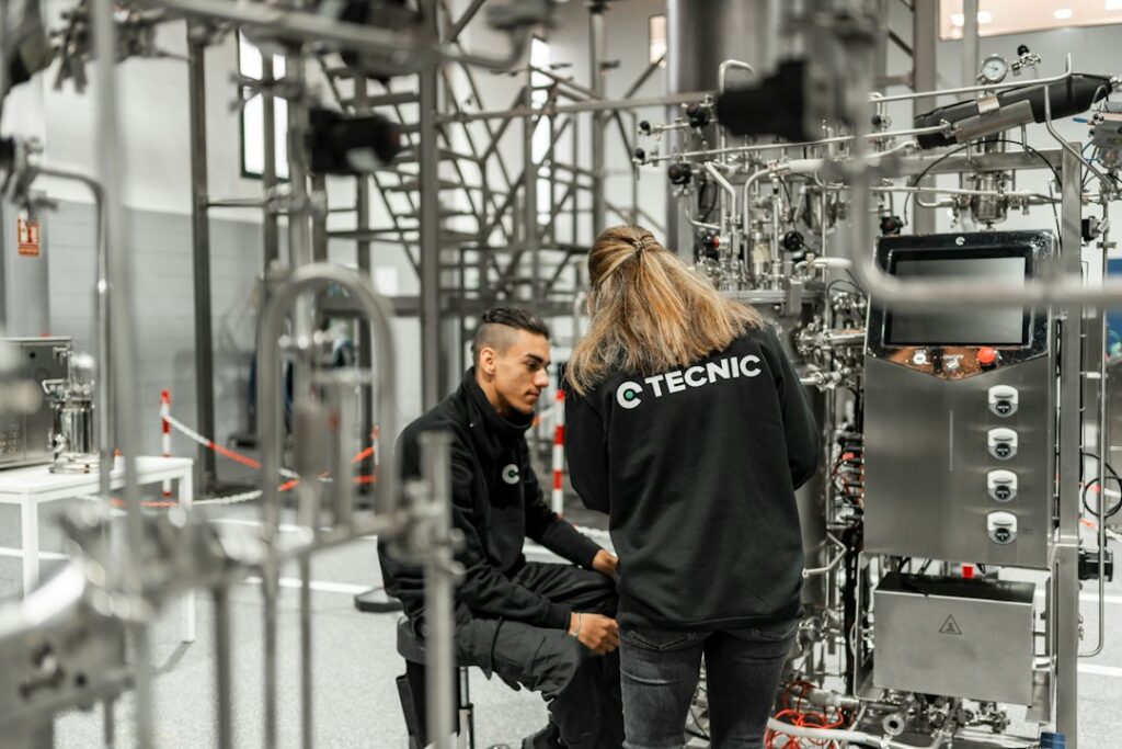 Due tecnici di imprese diverse controllano un impianto in acciaio in un locale tecnico, situazione tipica di interferenze da gestire nel DUVRI